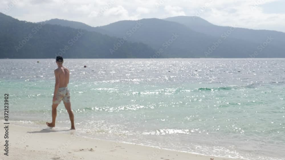 Ultra slow motion shot of young caucasian man walking relaxed with swimwear on stunning beach in Thailand Ultra slow motion shot of young caucasian man walking relaxed with swimwear on stunning beach in Thailand