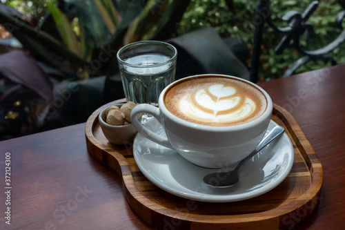 Cup of hot coffee on wooden tray with green garden background. Breakfast time.