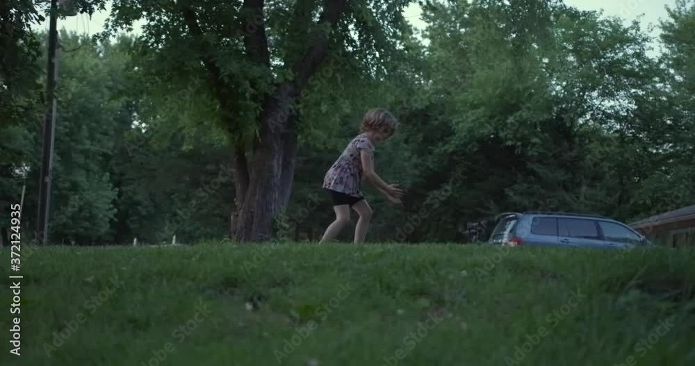 Low angle profile view of young cute innocent Caucasian girl walking and trying to catch lightning bugs by car in home backyard at dusk, handheld pan slow motion Low angle profile view of young cute innocent Caucasian girl walking and trying to catch lightning bugs by car in home backyard at dusk, handheld pan slow motion