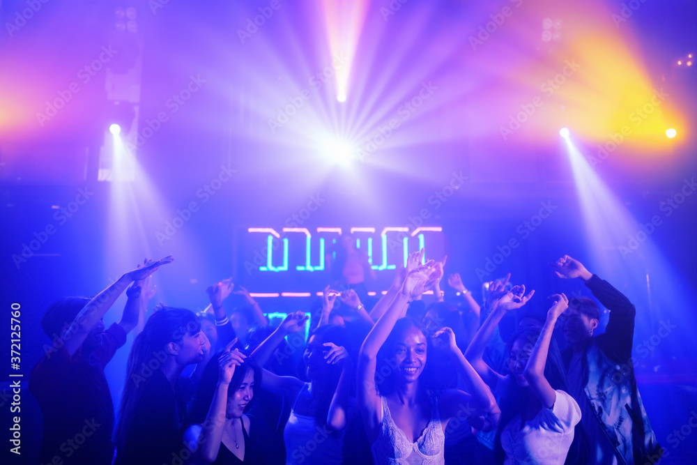 crowd of people raises hands dancing together on dancefloor in nightclub