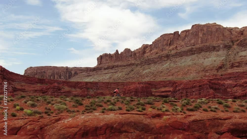 Aerial tracking shot of woman riding mountain bike on flat trail in red Moab desert Aerial tracking shot of woman riding mountain bike on flat trail in red Moab desert