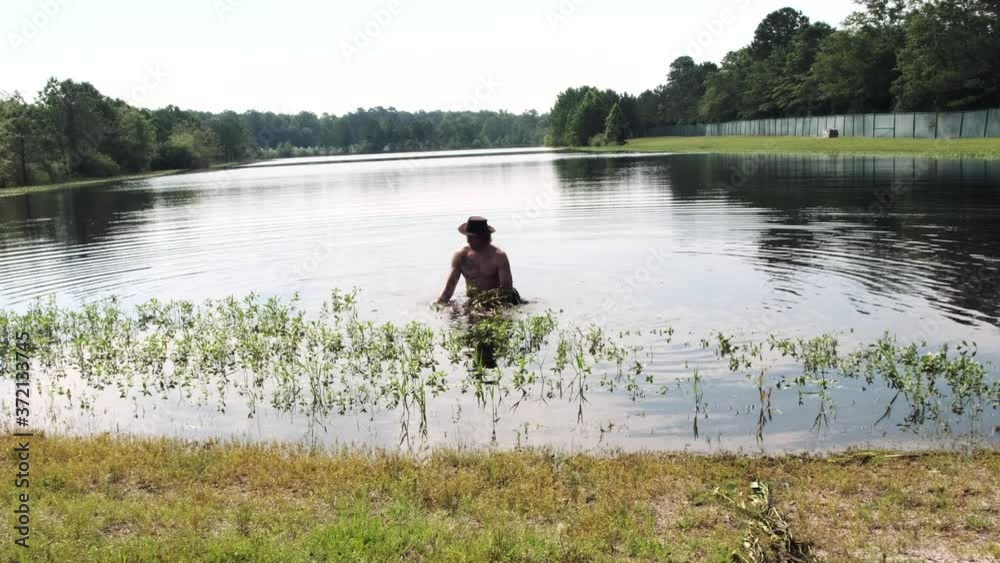 Healthy, muscular, shirtless Caucasian adult man with strong shoulders and physique wearing brown hat working in lake water pulling tall weeds from pond, static portrait Healthy, muscular, shirtless Caucasian adult man with strong shoulders and physique wearing brown hat working in lake water pulling tall weeds from pond, static portrait