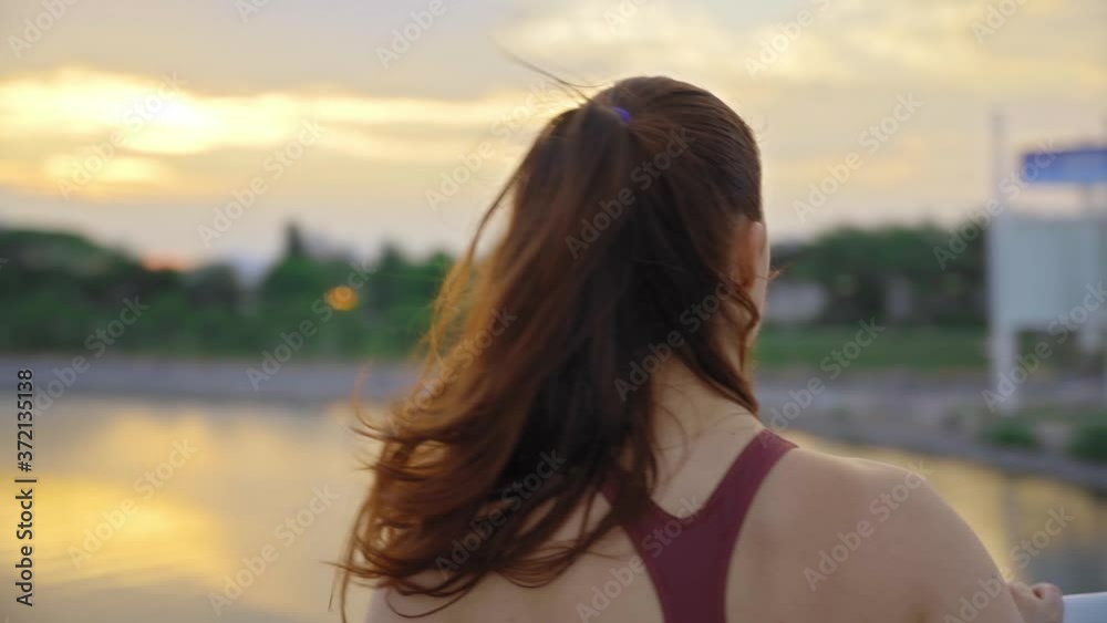 Beautiful happy athletic redhead woman looking at the sunset by the lake on a bridge Beautiful happy athletic redhead woman looking at the sunset by the lake on a bridge