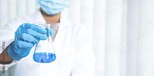 Scientists hold a glass tube filled with blue chemical liquid for research and analysis in a laboratory
