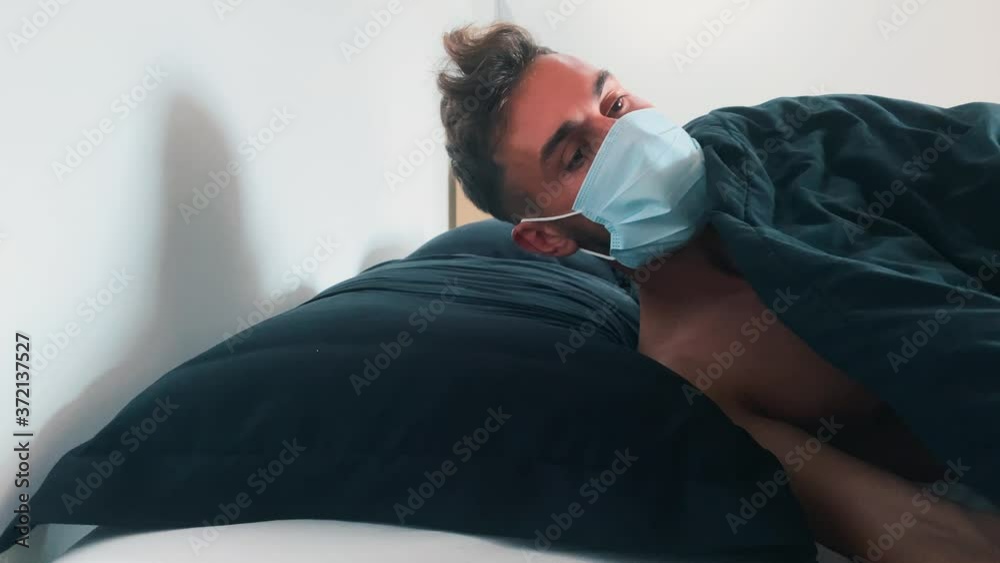 Young caucasian male going to sleep wearing face mask lying in bed, COVID-19