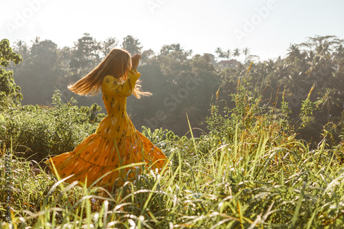 Summertime and lifestyle. Young unrecognizable carefree woman enjoying dancing freedom and sunny nature scene. Picturesque view of countryside at background.. © Yevhenii