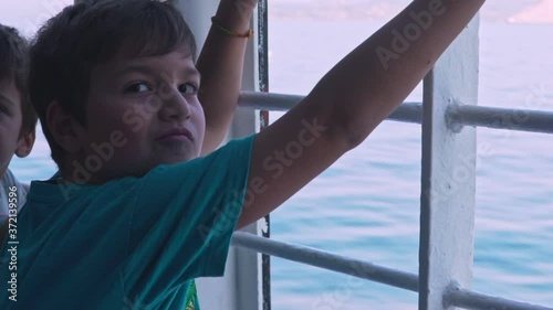 Close up of two caucasian kids standing at gunwale of a ferry boat, traveling at Argosaronikos sea, Greece 120fps photo