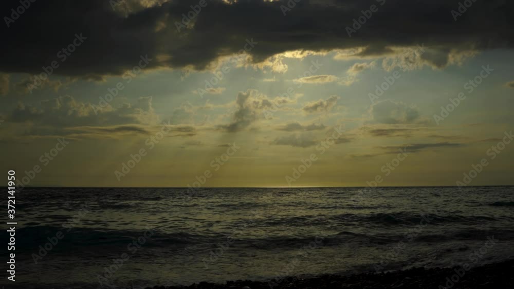 Dramatic seascape with dark clouds covering sunset and sun rays reflecting on sea surface Dramatic seascape with dark clouds covering sunset and sun rays reflecting on sea surface