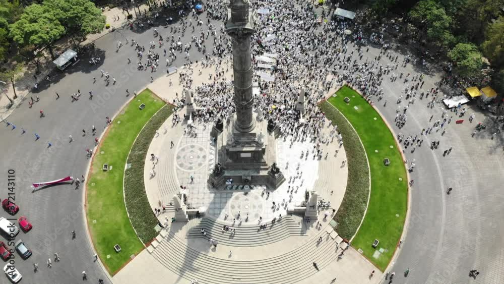 Vista aérea de una multitud de personas manifestandose sobre el Paseo de la Reforma en la Ciudad de México. El drone volando atras del Angel de la Independencia
