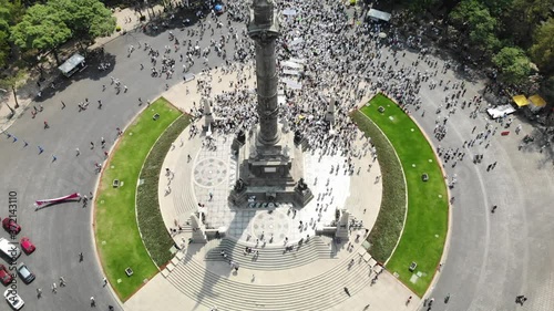 Vista aérea de una multitud de personas manifestandose sobre el Paseo de la Reforma en la Ciudad de México. El drone volando atras del Angel de la Independencia
