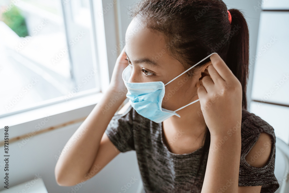 Close up of teenage girl is wearing a mask while sitting by the window in the room before going out