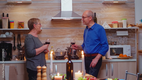 Huband and wife discussing about funny things after romantic dinner. Senior old couple drinking wine and talking, sitting near kitchen table, celebrating their anniversary in the dining room. photo