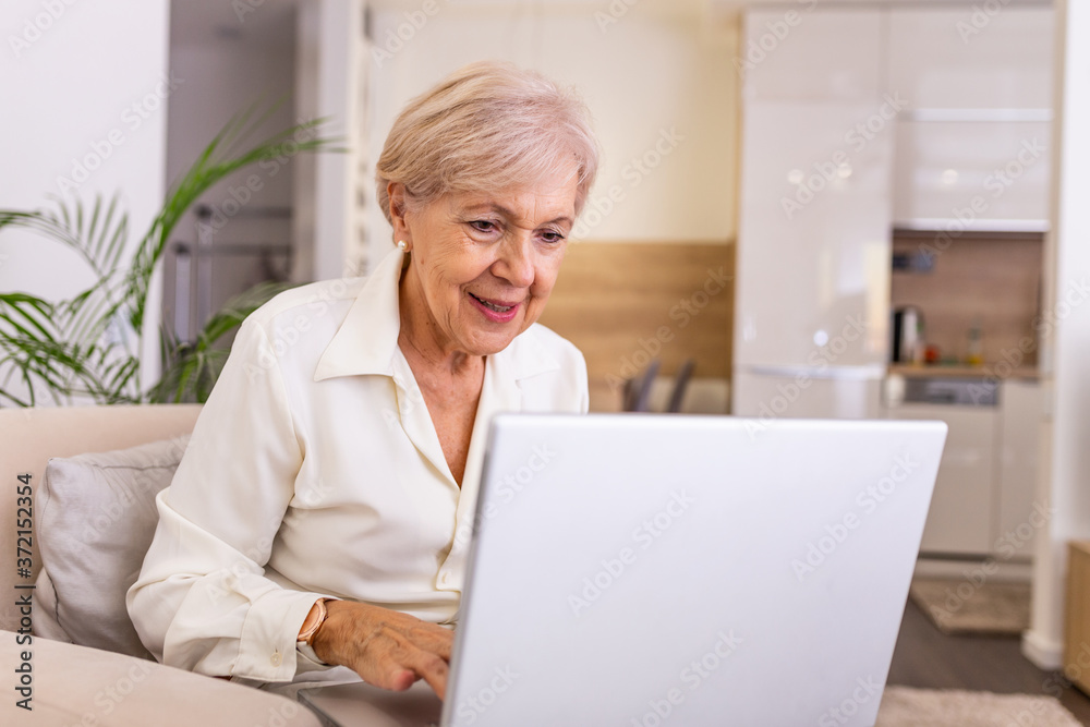Elderly lady working with laptop. Portrait of beautiful older woman working laptop computer indoors. Senior woman using laptop at home, laughing Elderly lady working with laptop. Portrait of beautiful older woman working laptop computer indoors. Senior woman using laptop at home, laughing