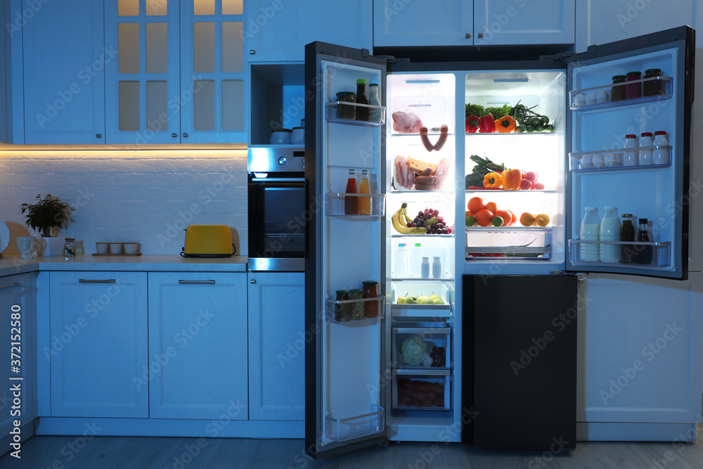 Open refrigerator filled with food in kitchen at night Open refrigerator filled with food in kitchen at night