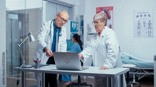 Фотография Two elderly senior experienced doctors deciding patient treatment while nurse is working in background