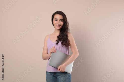Young woman with laptop on beige background
