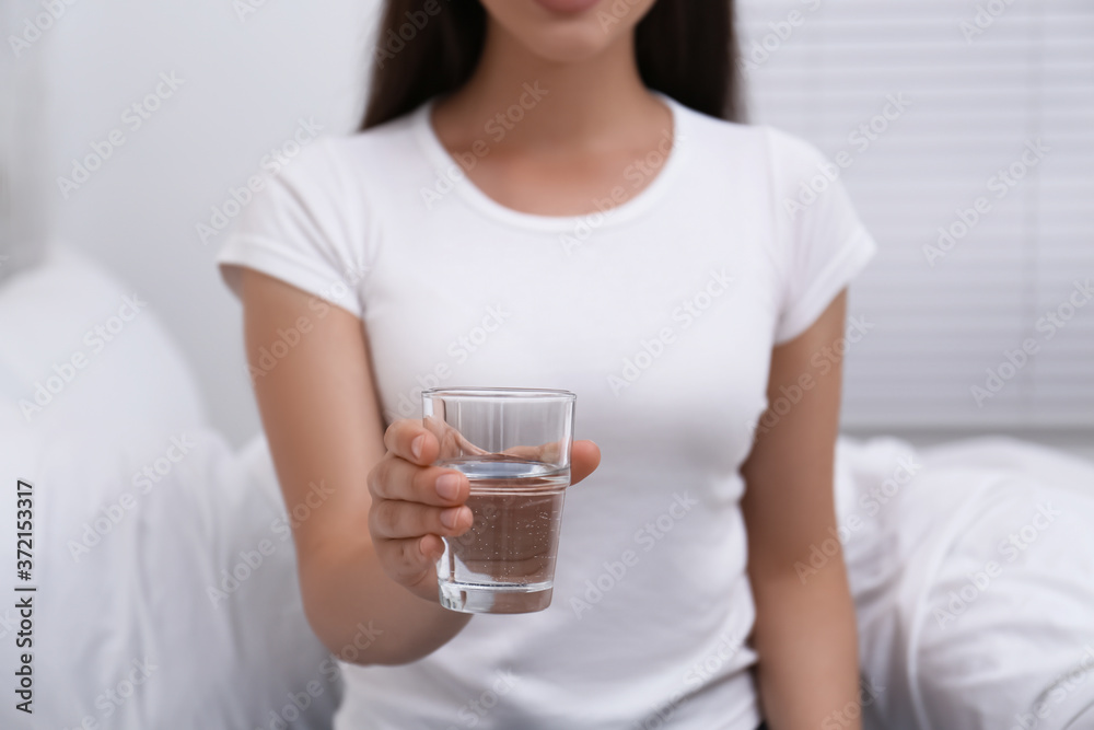Woman holding glass of water in bedroom, closeup Woman holding glass of water in bedroom, closeup