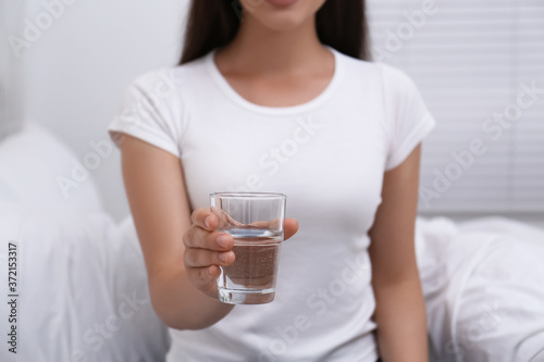 Woman holding glass of water in bedroom, closeup