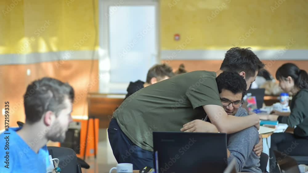 two men hug in coworking open space office, greeting friends irrl. colleagues embrace while working at laptop. college students team in coworking space. concept workplace, corporate two men hug in coworking open space office, greeting friends irrl. colleagues embrace while working at laptop. college students team in coworking space. concept workplace, corporate