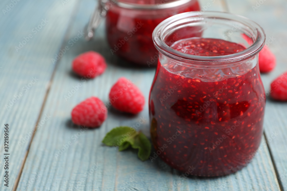 Delicious jam and fresh raspberries on light blue wooden table, closeup