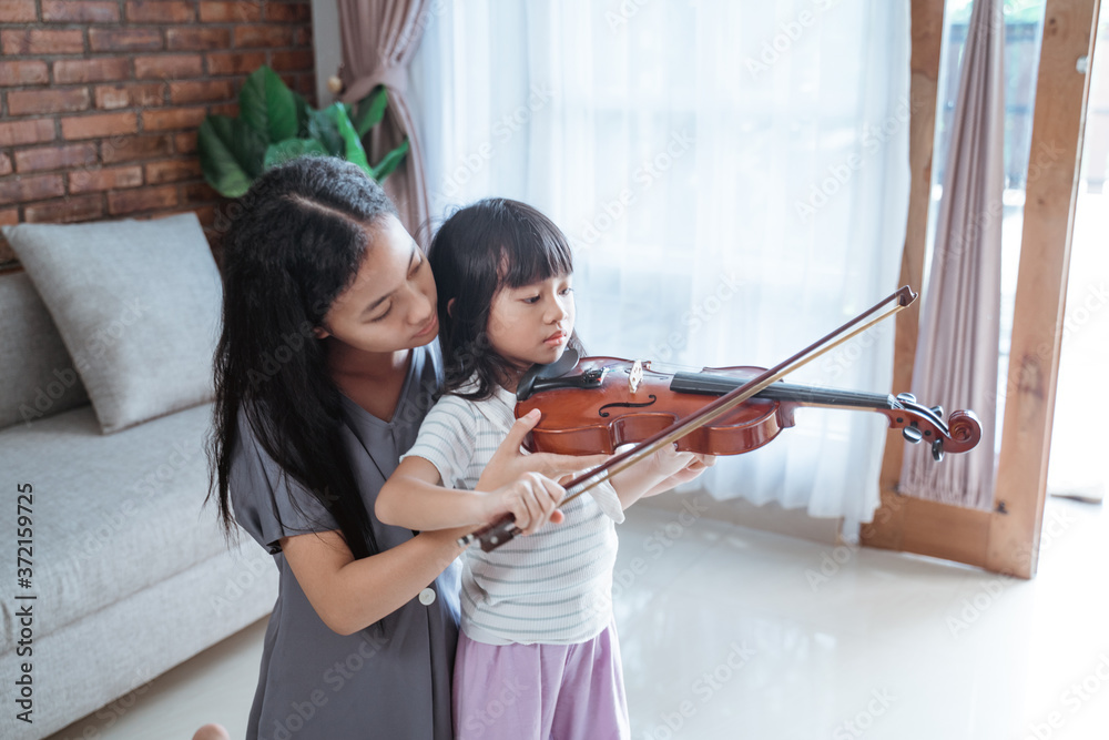 little girl assisted by teenage girl hold the violin properly while learn playing the violin indoors against the background of the window little girl assisted by teenage girl hold the violin properly while learn playing the violin indoors against the background of the window