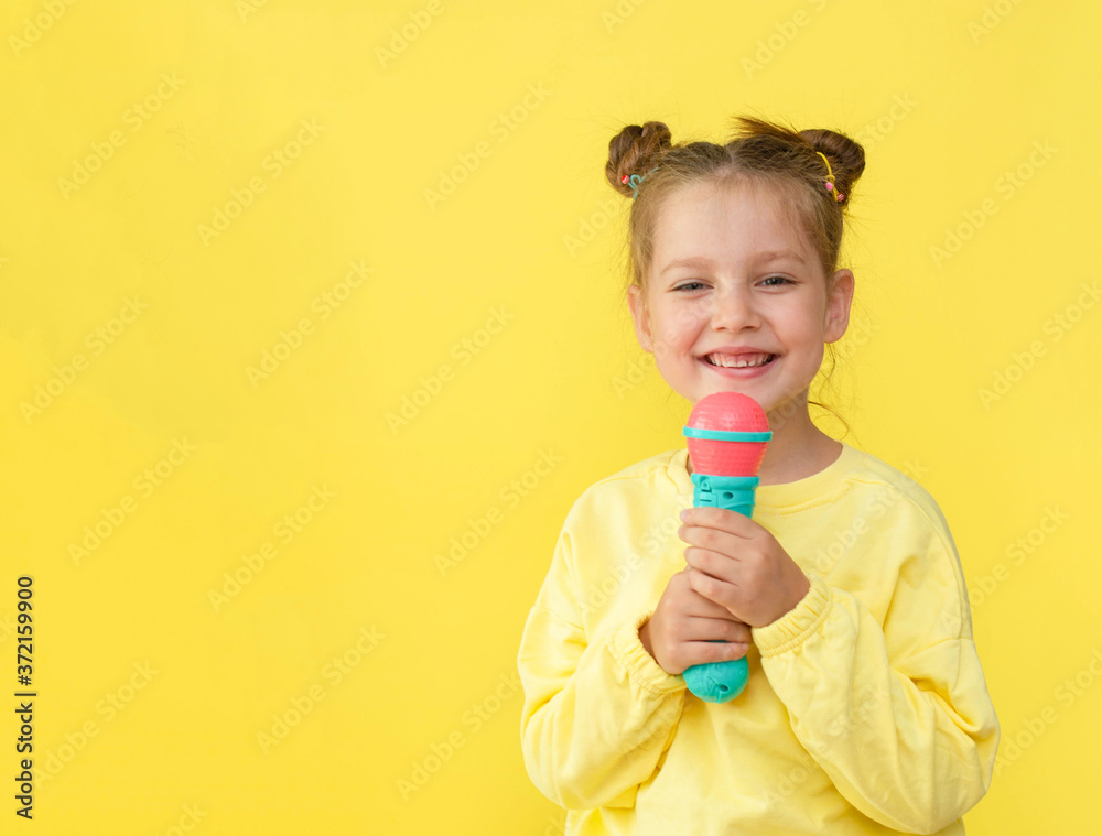 Lifestyle and people concept: a small, happy girl singing with a microphone, isolated by a bright yellow background. Lifestyle and people concept: a small, happy girl singing with a microphone, isolated by a bright yellow background.