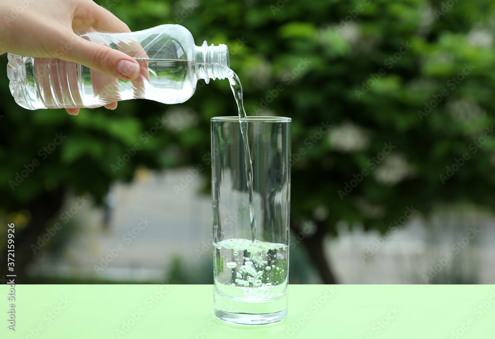 Woman pouring water from bottle into glass on table outdoors, closeup Woman pouring water from bottle into glass on table outdoors, closeup