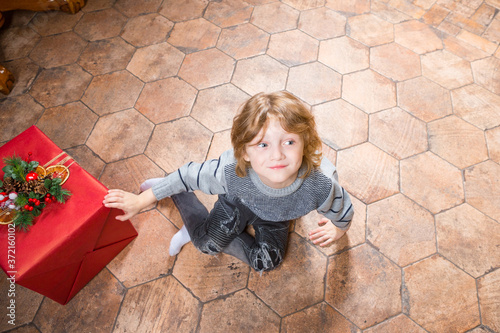 smiling wearing in grey sweater, jeans and white socks man-child with huge red handsel sits on a floor photo