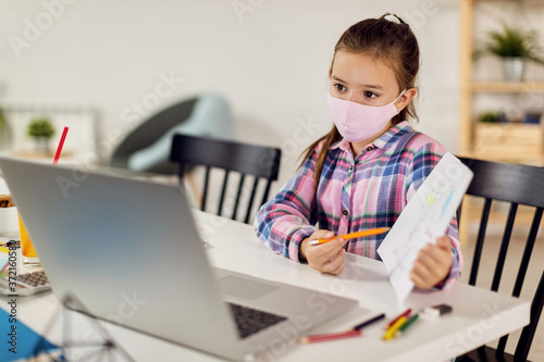 Schoolgirl with face mask having online video class at home during coronavirus lockdown.