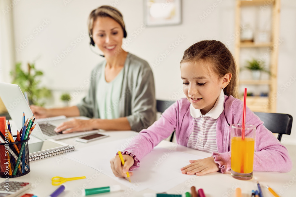 Happy girl drawing on paper while her mother is working at home.