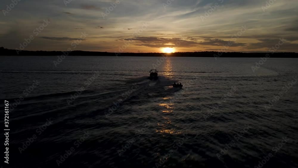 Drone chasing speedboat while towing people. A sweeping shot of boat on the lake at sunset. Drone chasing speedboat while towing people. A sweeping shot of boat on the lake at sunset.