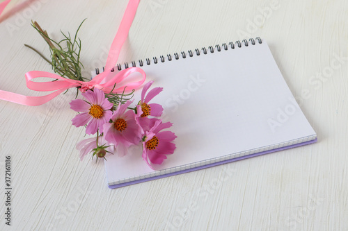 Notepad with a bouquet of delicate pink flowers, place for writing, top view