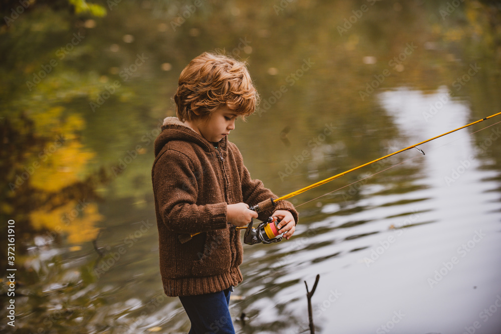 Little fisherman. Child boy fishing in overalls from a dock on lake or  pond. Stock Photo