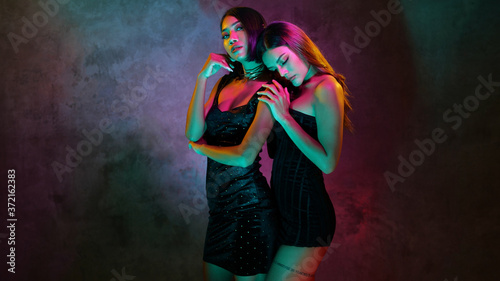 Portrait of two young cute Asian women in elegant dresses on the pink and yellow neon lights