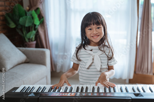 cute little girl wit smile plays a keyboard instrument in a room at home with curtain background
