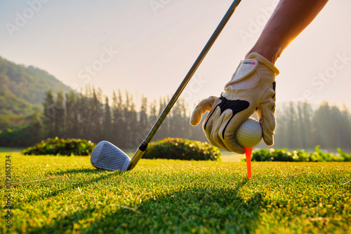 Close up Hand asian woman putting golf ball on tee with club in golf course on sunny day for healthy sport. Lifestyle Concept.
