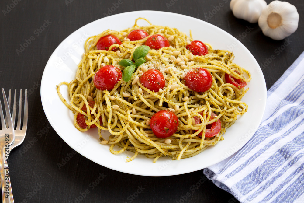 Homemade Pesto Pasta with Tomatoes and Pine Nuts on a black surface, low angle view. Homemade Pesto Pasta with Tomatoes and Pine Nuts on a black surface, low angle view.