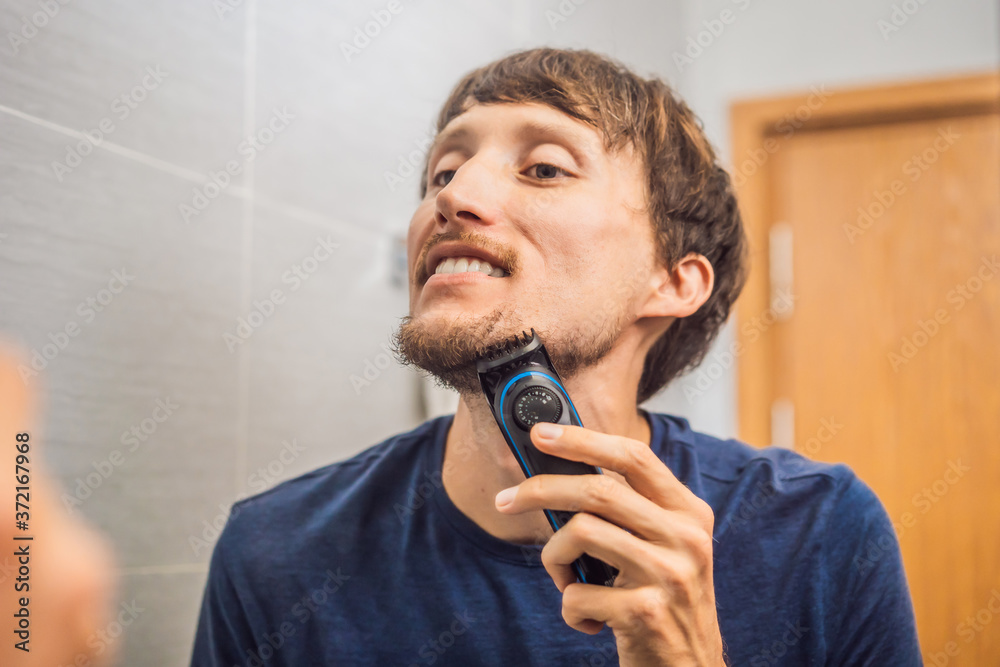 Handsome young bearded man trimming his beard with a trimmer Handsome young bearded man trimming his beard with a trimmer