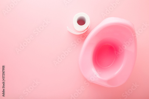 Baby potty and white toilet paper roll on light pink table background. Pastel color. Hygiene concept. Closeup. Empty place for text. Top down view. photo