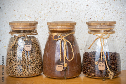Coffee beans, ground coffee and green coffee in glass jars on a table.