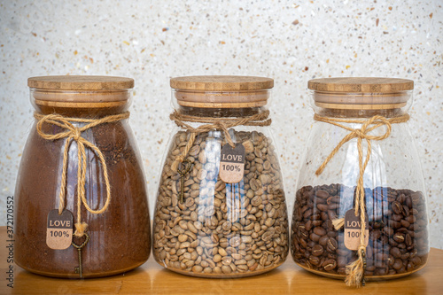 Coffee beans, ground coffee and green coffee in glass jars on a table.