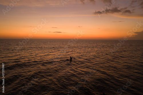 Surfer silhouette into the ocean waves at sunrise. Bali