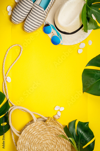 Straw hat, camera, bag, summer shoes, sunglasses, shells and tropical leaves over yellow background