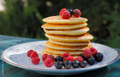 Pancakes. A stack of pancakes on a white plate garnished with raspberries and black currants. Food background. Horizontal, side view, close-up, free space.