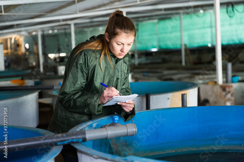 Woman owner of trout farm checking reservoirs with fry, writing results of inspection in notebook.. © JackF