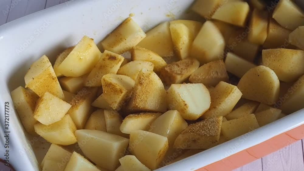 Potatoes in a ceramic baking dish with spices are mixed with a spoon. Potatoes in a ceramic baking dish with spices are mixed with a spoon.