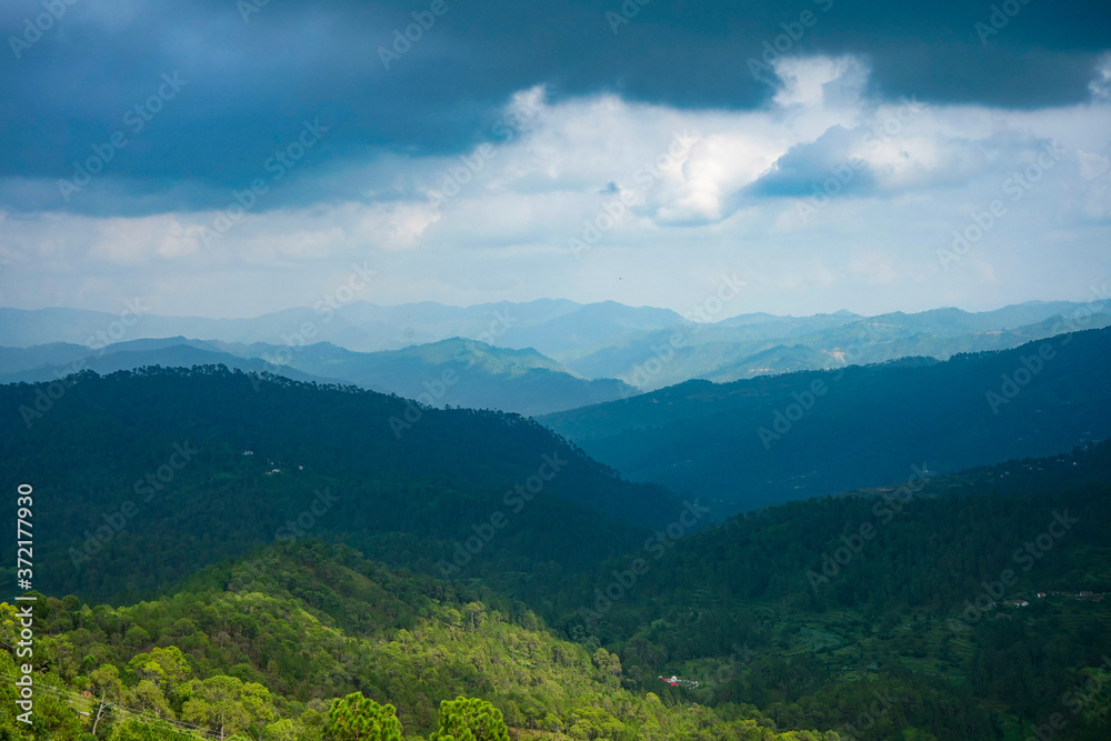 A beautiful and soothing landscape of mountains covered in clouds and green trees during winters.