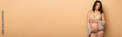 horizontal concept of young pregnant woman in lingerie posing on beige