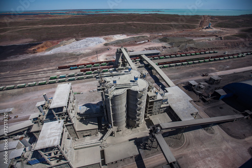 Mynaral/Kazakhstan: Modern cement plant in desert. Cement silos. Hopper cars on railroad terminal. Railway carriages on track.