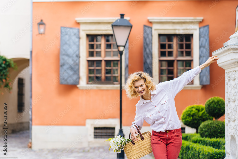 Portrait of romantic mature slim blonde woman in white shirt red pants enjoying, walking outdoor in cozy yard or street in summer time outdoor. Vacation in your country, slow living concept. Portrait of romantic mature slim blonde woman in white shirt red pants enjoying, walking outdoor in cozy yard or street in summer time outdoor. Vacation in your country, slow living concept.